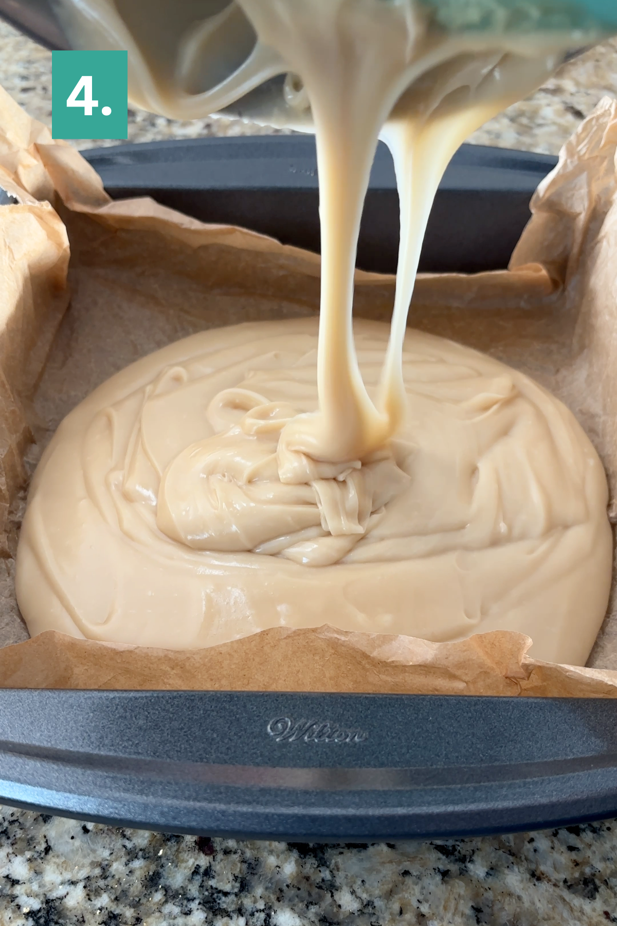 Thick, creamy caramel apple fudge batter is being poured into a parchment-lined baking pan on a granite countertop. A teal box labeled 4. is in the upper left corner, indicating a recipe step.