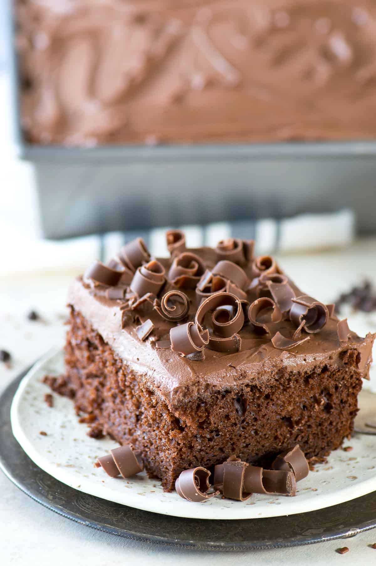 slice of chocolate cake with chocolate frosting and chocolate curls on white plate