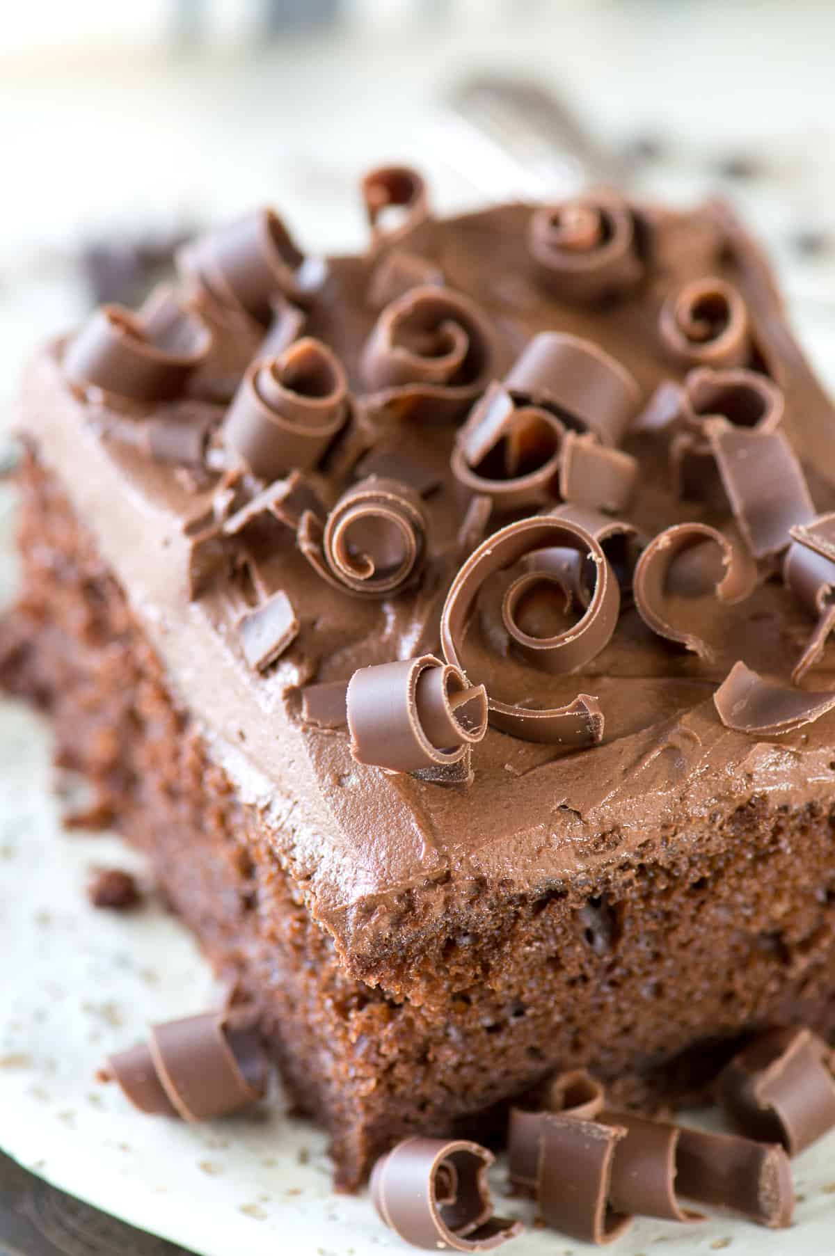 slice of chocolate cake with chocolate frosting and chocolate curls on white plate
