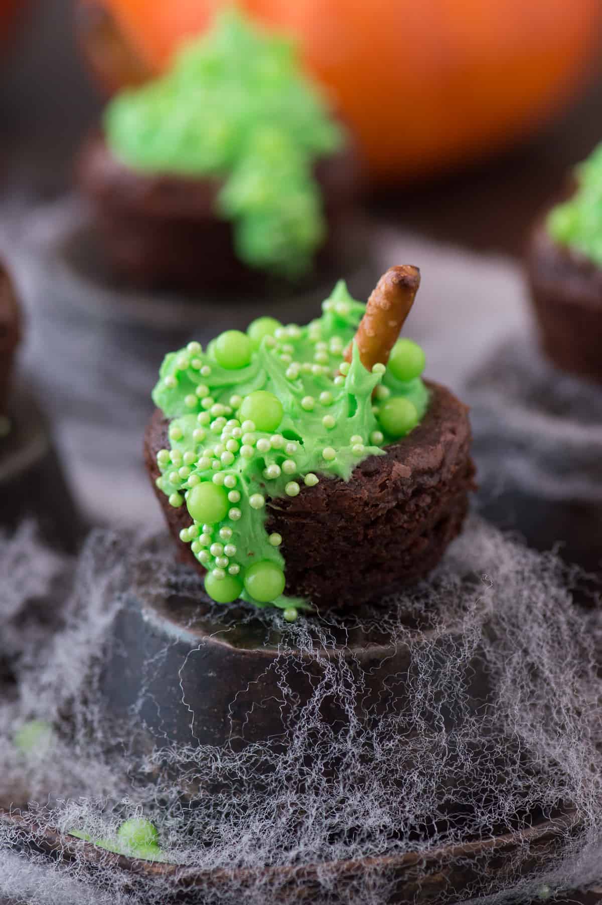 mini brownie bites filled with green frosting and green sprinkles to look like a bubbling witch's cauldron