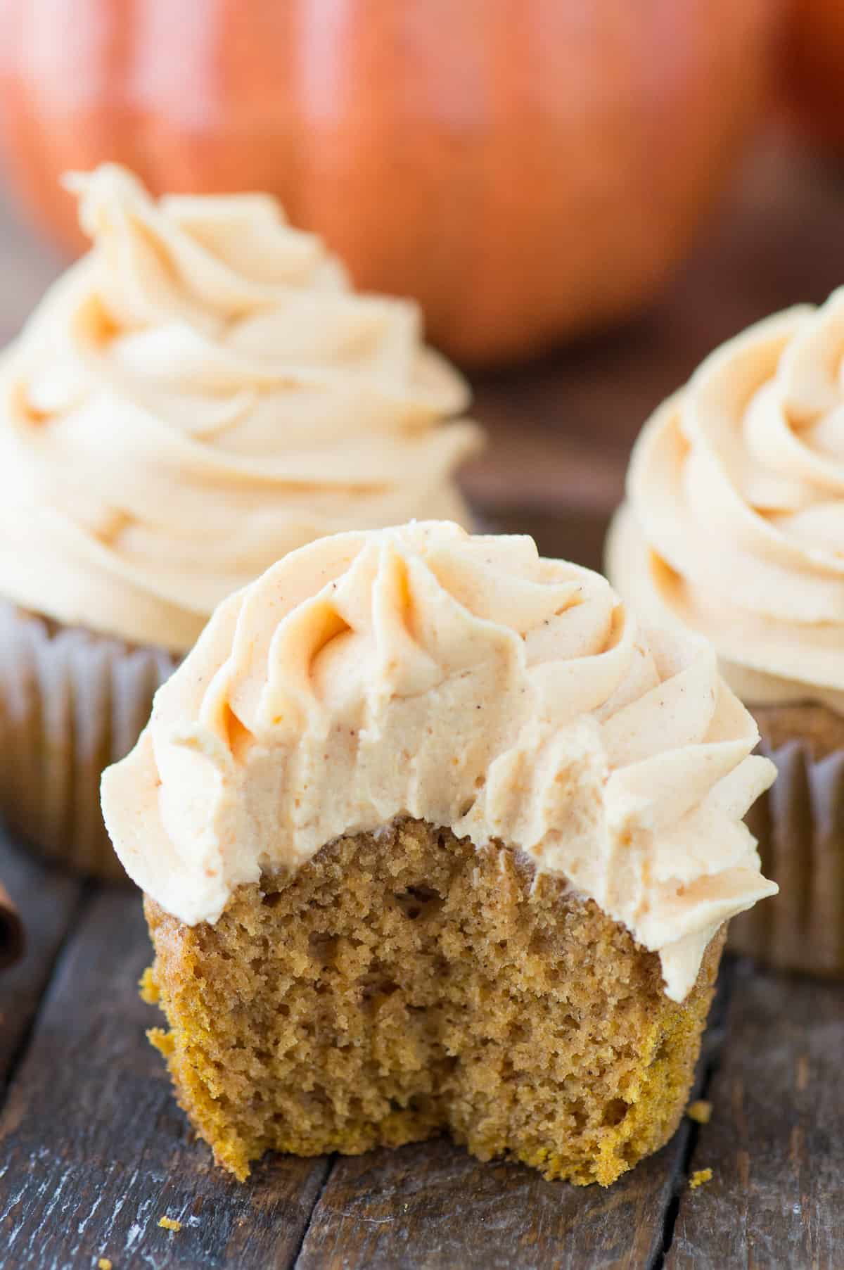 pumpkin cupcake piped with pumpkin frosting with bite removed on wood background