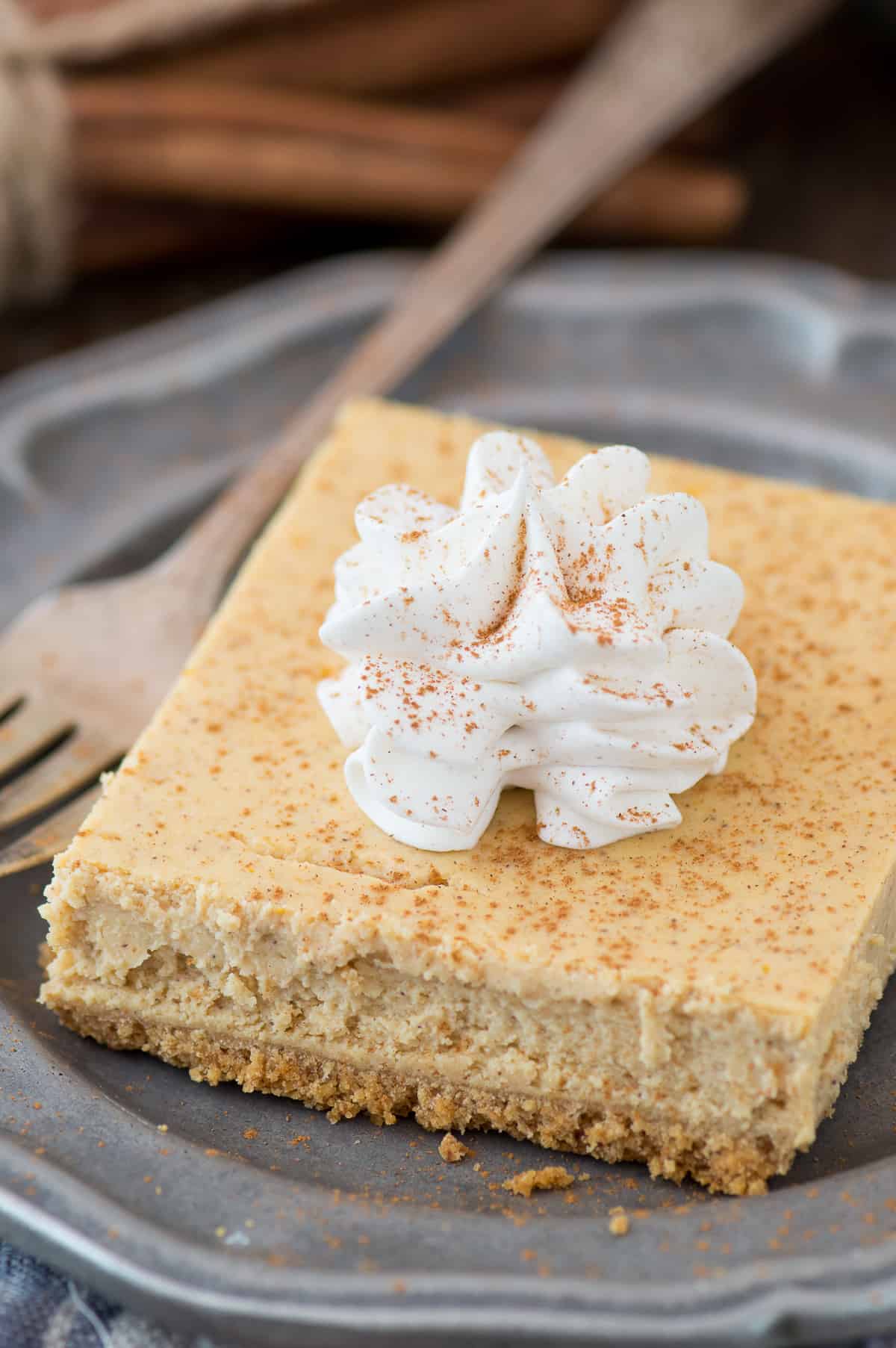 slice of pumpkin cheesecake bar with dollop of whipped cream on top on metal plate