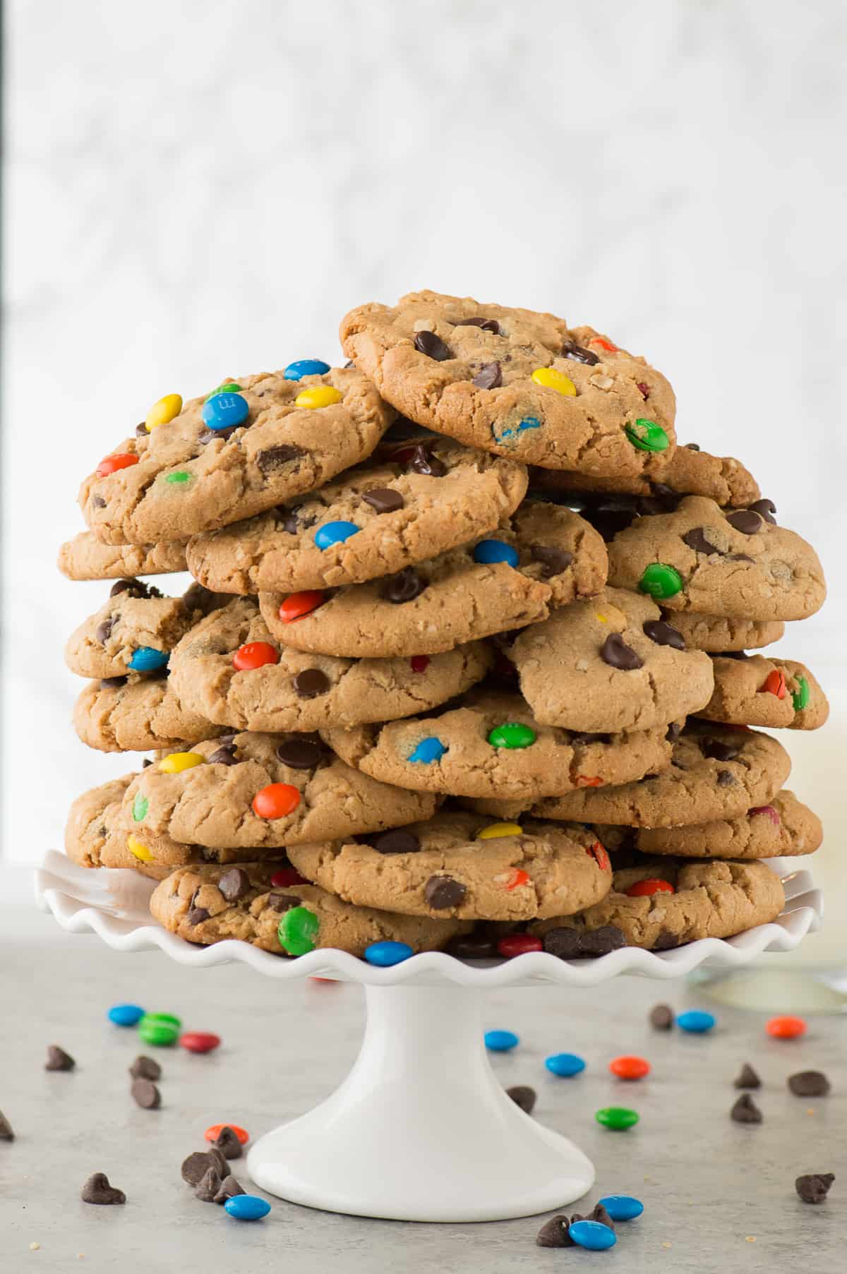 monster cookies in a giant stack on a white cake stand