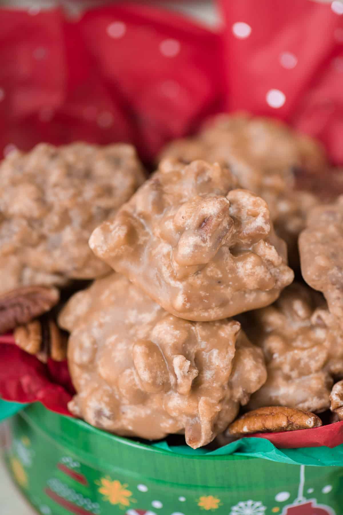 pecan pralines arranged in a pile in christmas tin with red tissue paper