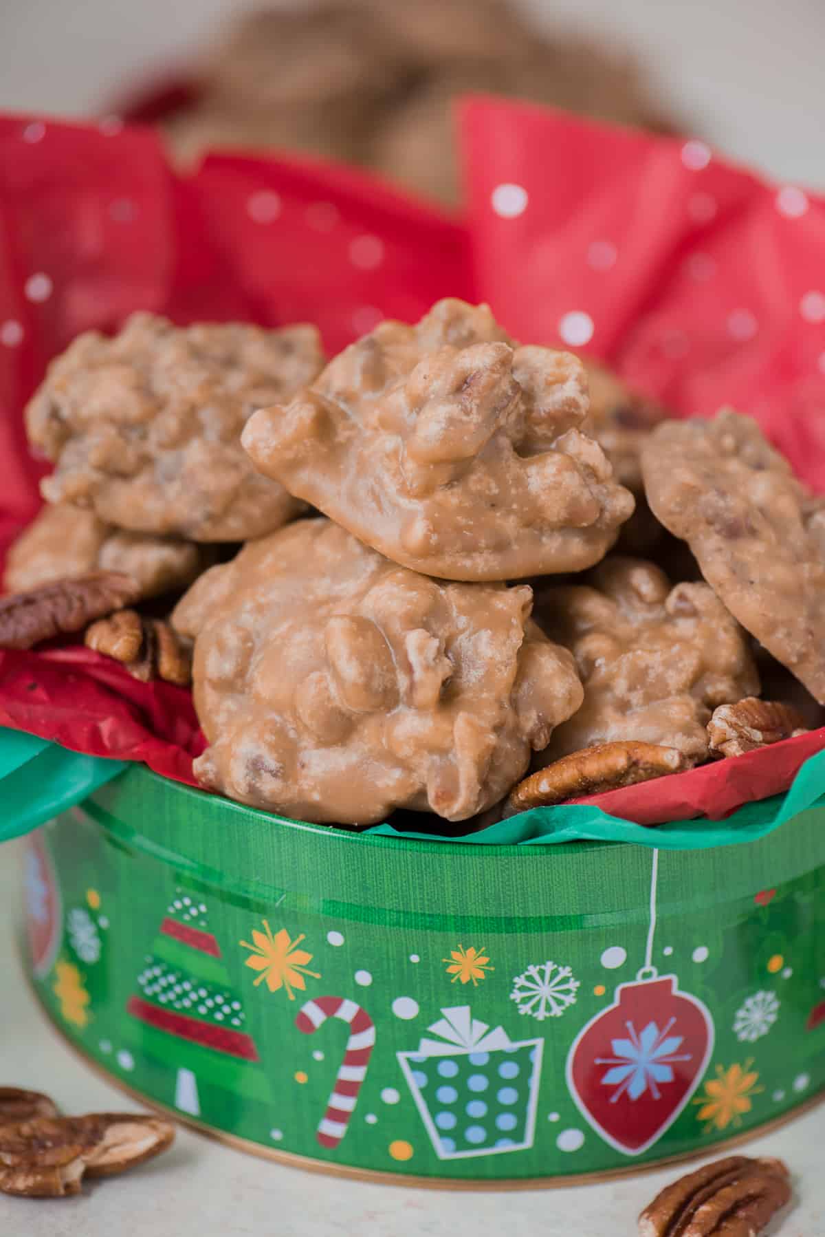 pecan pralines arranged in a pile in christmas tin with red tissue paper