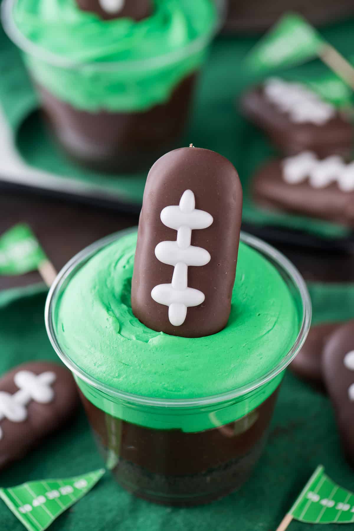 Homemade Football themed dirt cups with bright green frosting on a green napkin.