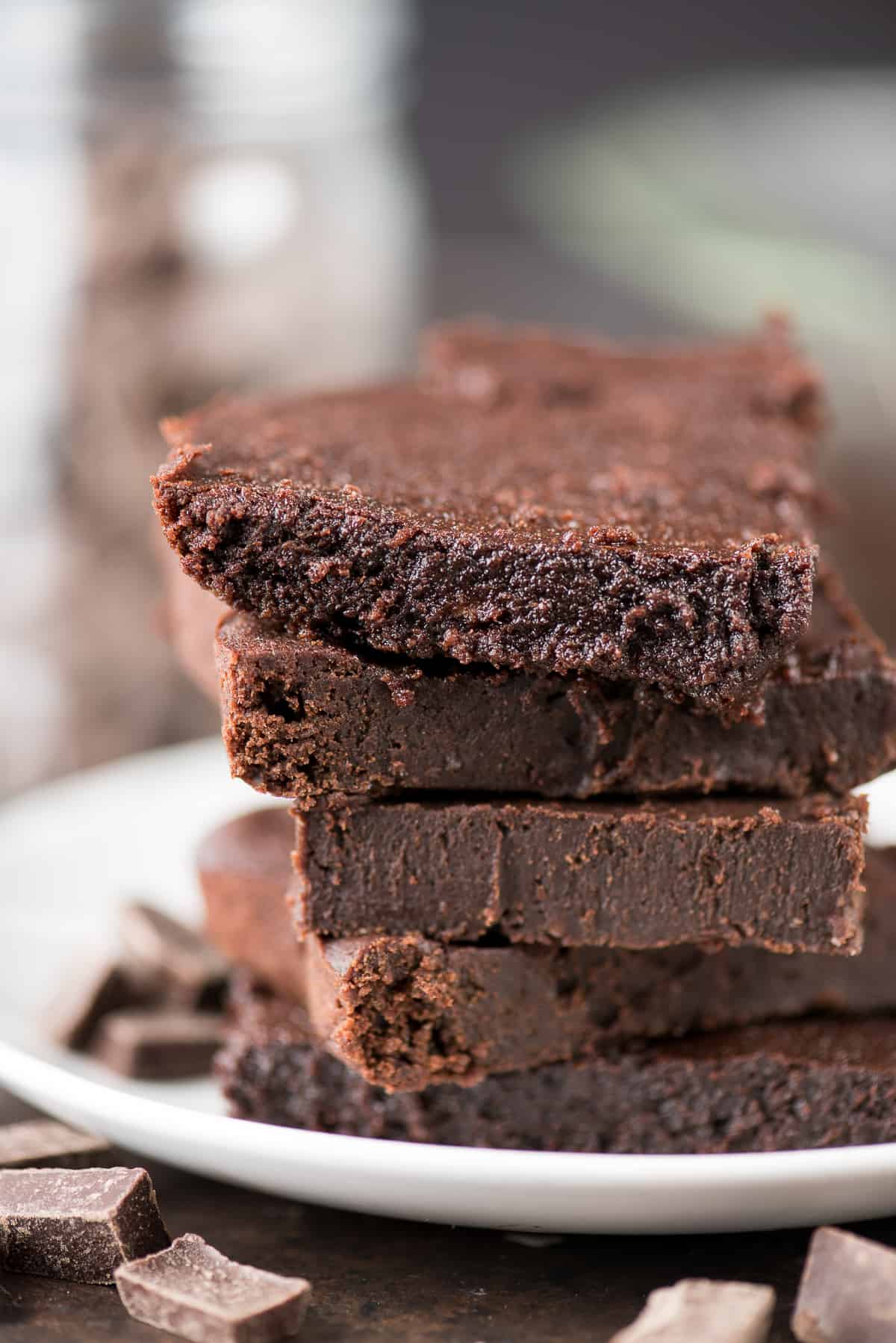 Five healthier fudgy brownies surrounded by chocolate on a white plate.