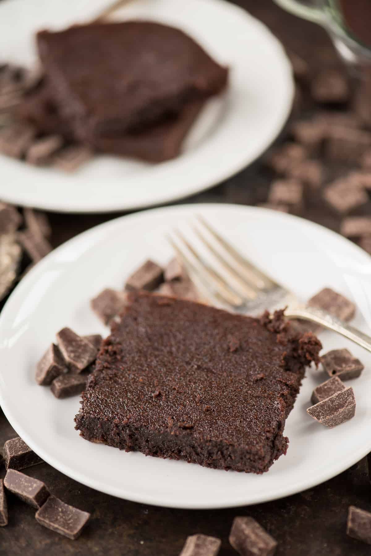 One healthier fudgy brownie with small chocolate and a silver fork on a white plate.