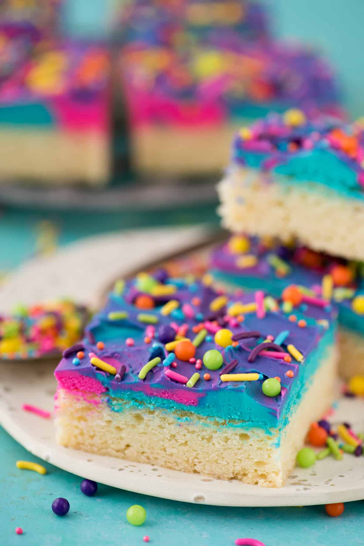 a sugar cookie bar on a white plate with blue, pink and purple frosting and multi color sprinkles