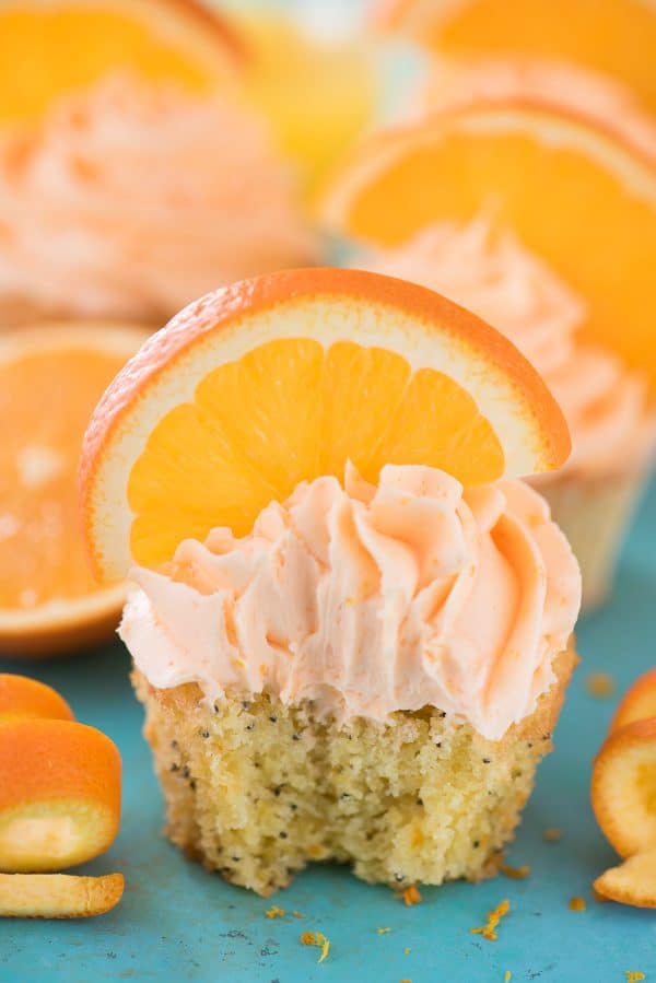 Orange Poppy Seed Cupcakes are a unique citrus cupcake recipe. They are made with real orange juice and orange zest! Orange Poppy Seed Cupcake with orange slice on blue background