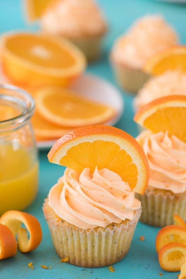 Orange Poppy Seed Cupcakes are a unique citrus cupcake recipe. They are made with real orange juice and orange zest! Orange Poppy Seed Cupcake with orange slice on blue background