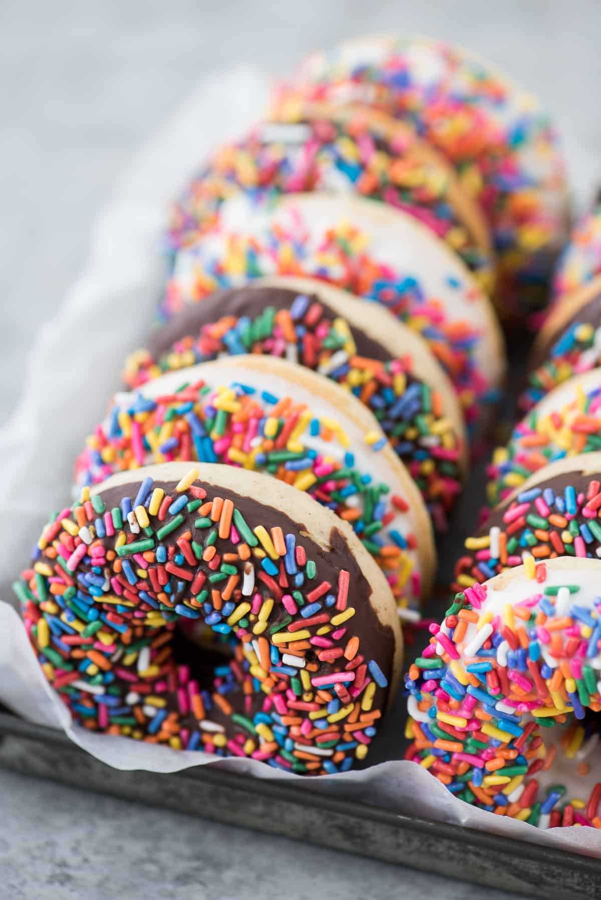 donuts with chocolate and white chocolate glaze with rainbow sprinkles lined up in metal pan