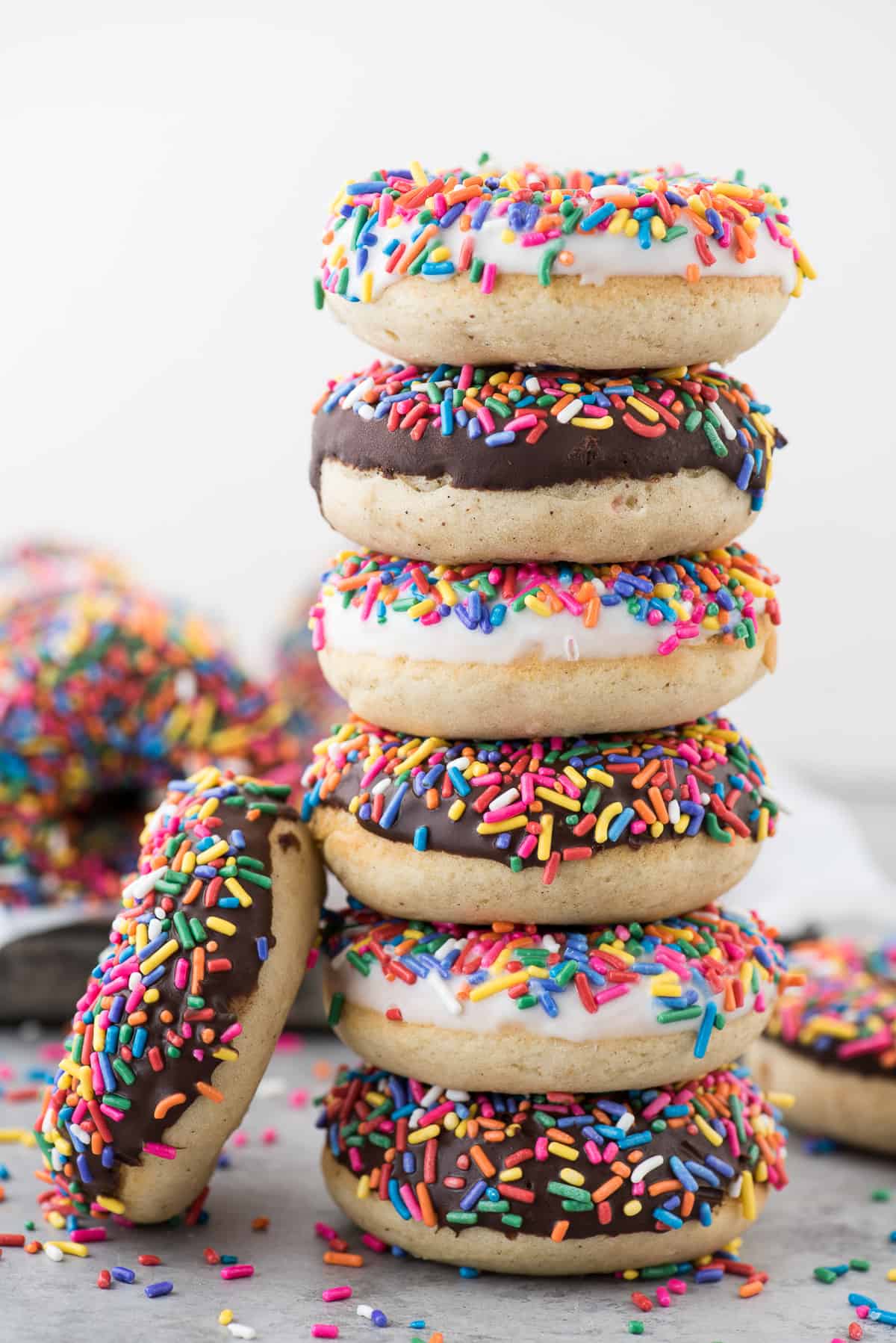 6 donuts with chocolate and white chocolate glaze with rainbow sprinkles stacked on each other