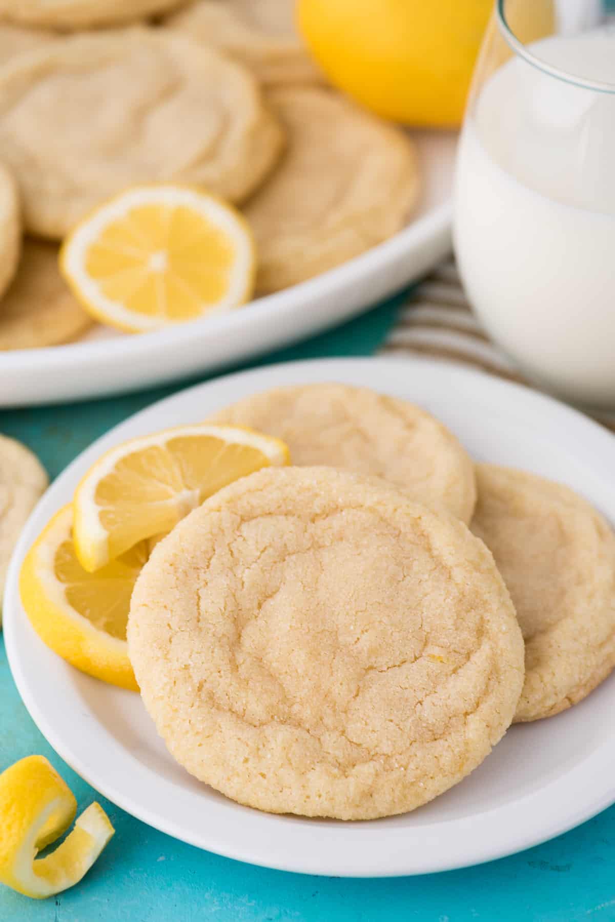 lemon cookies on white plate with glass of milk on blue background