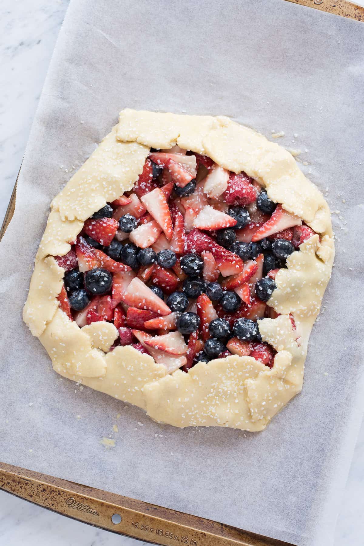 mixed berry galette with strawberries and blueberries on metal baking sheet before baking the pie