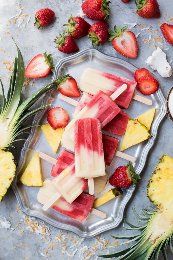 The best miami vice mocktail popsicles! Half strawberry daiquiri half pina colada. These are tropical, lava flow popsicles that everyone can enjoy since they are non-alcoholic. strawberry and coconut layered popsicles on metal tray on gray background