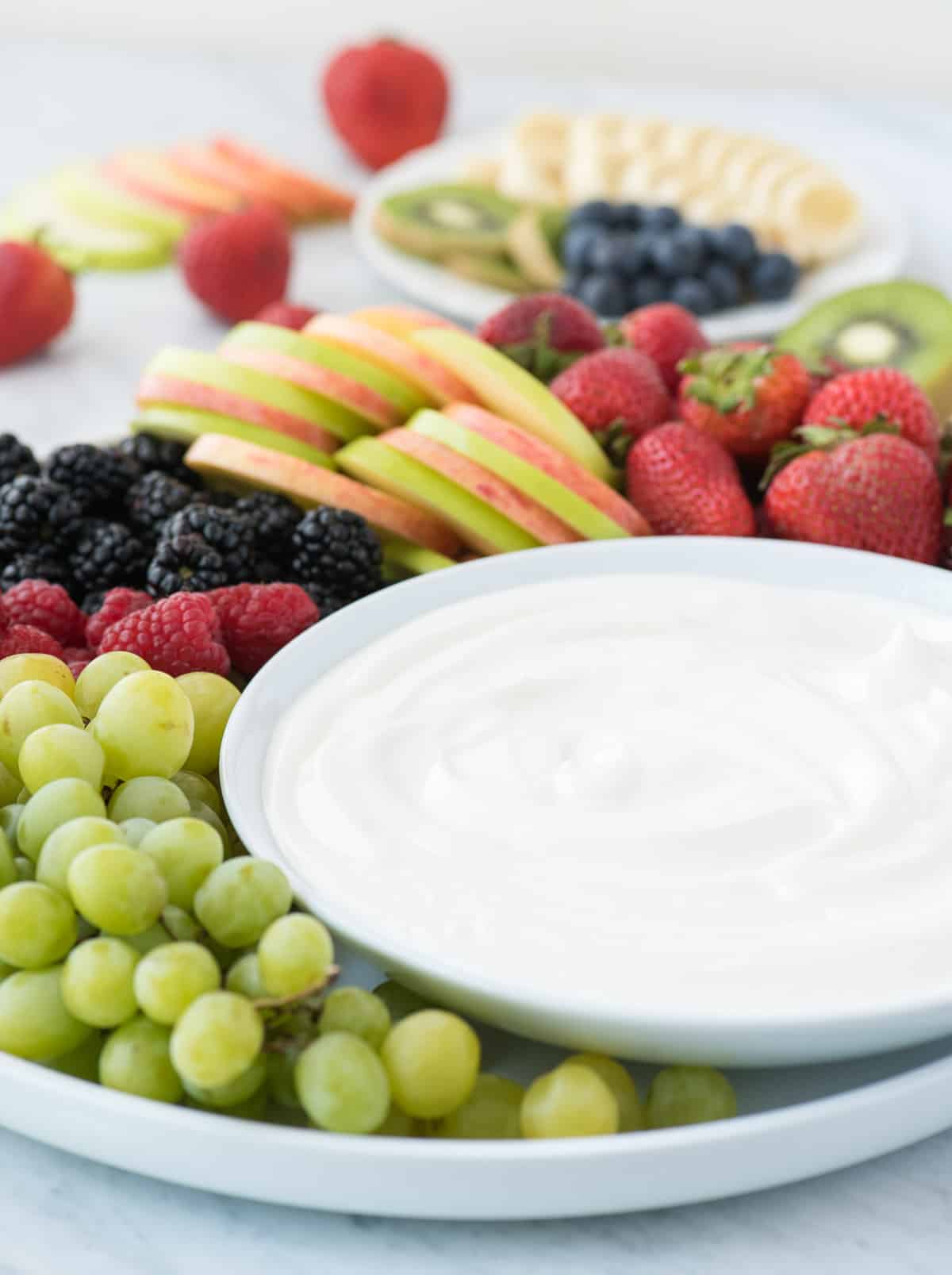 round platter filled with strawberries, apples, blackberries, raspberries and grapes with a bowl of white fruit dip 