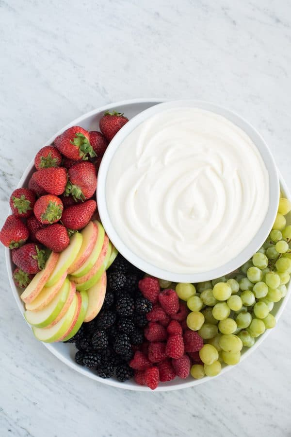 3 ingredient fruit dip! We love this creamy dip because there’s NO cream cheese! round platter filled with strawberries, apples, blackberries, raspberries and grapes with a bowl of white fruit dip