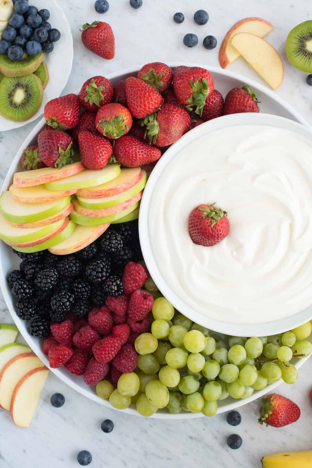round platter filled with strawberries, apples, blackberries, raspberries and grapes with a bowl of white fruit dip 