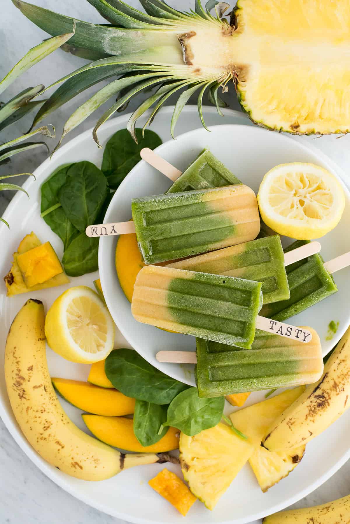 Green spinach and mango layered popsicles with fruit on a white platter