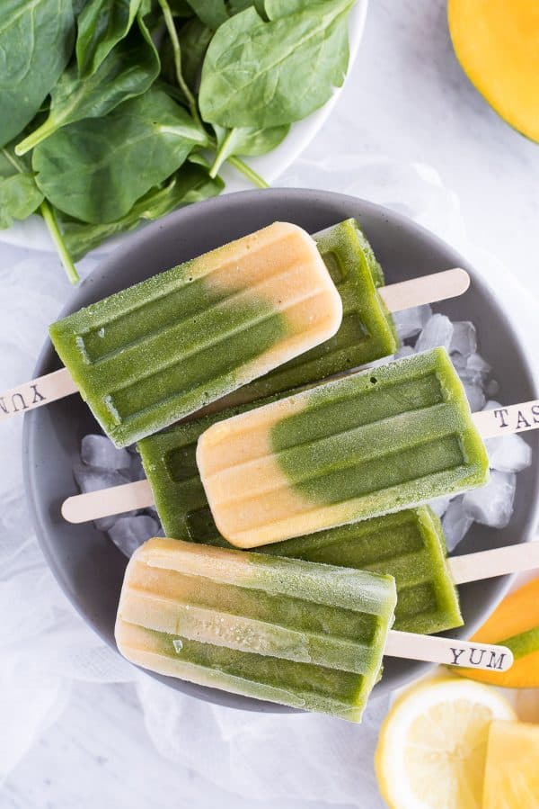 These Green Machine Popsicles are dairy free and customizable with different fruit options! Healthy popsicle recipe. #popsicles Green spinach and mango layered popsicles in a gray bowl on a white background