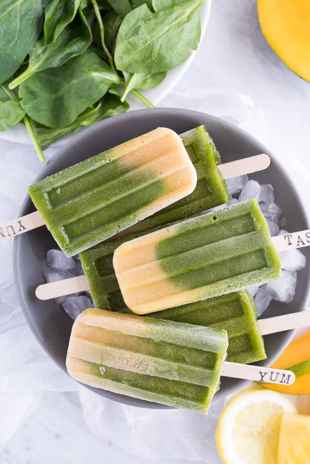 Green spinach and mango layered popsicles in a gray bowl on a white background