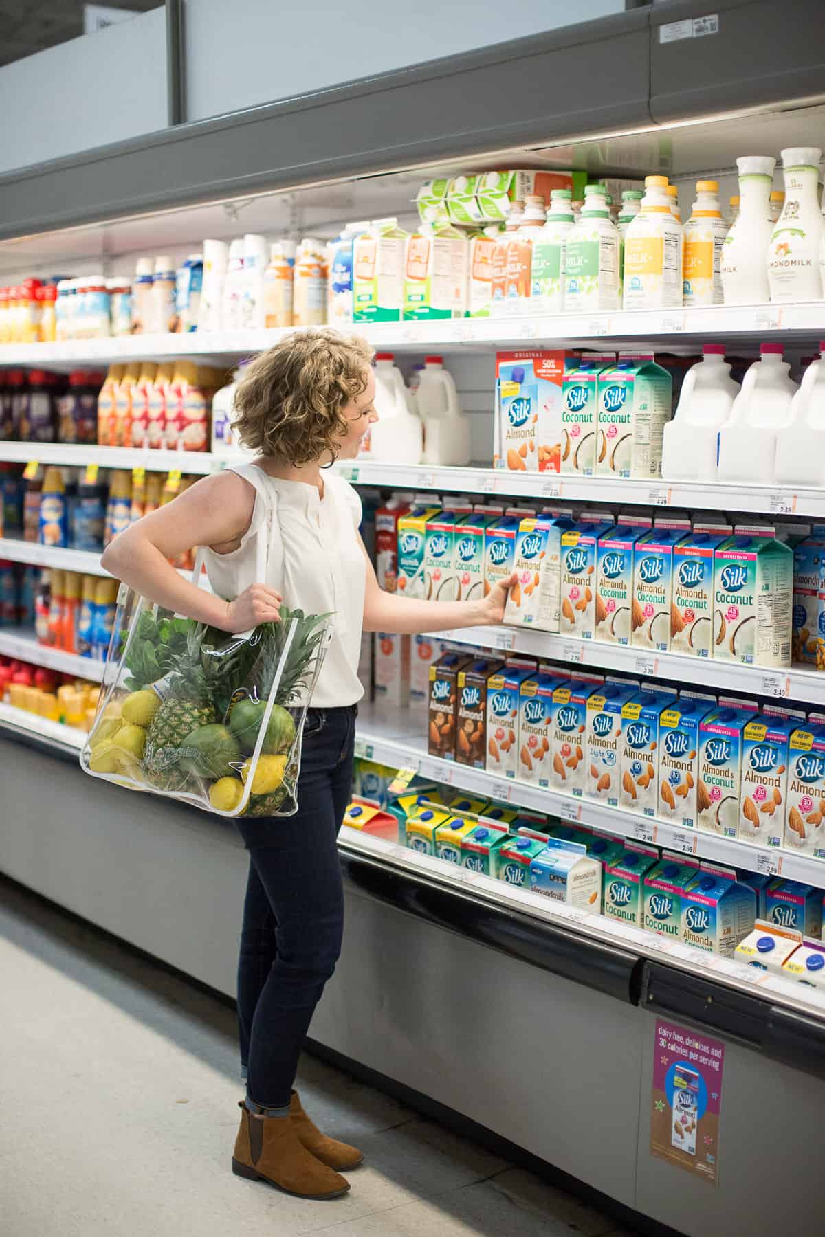 Woman standing in grocery store reaching for almondmilk