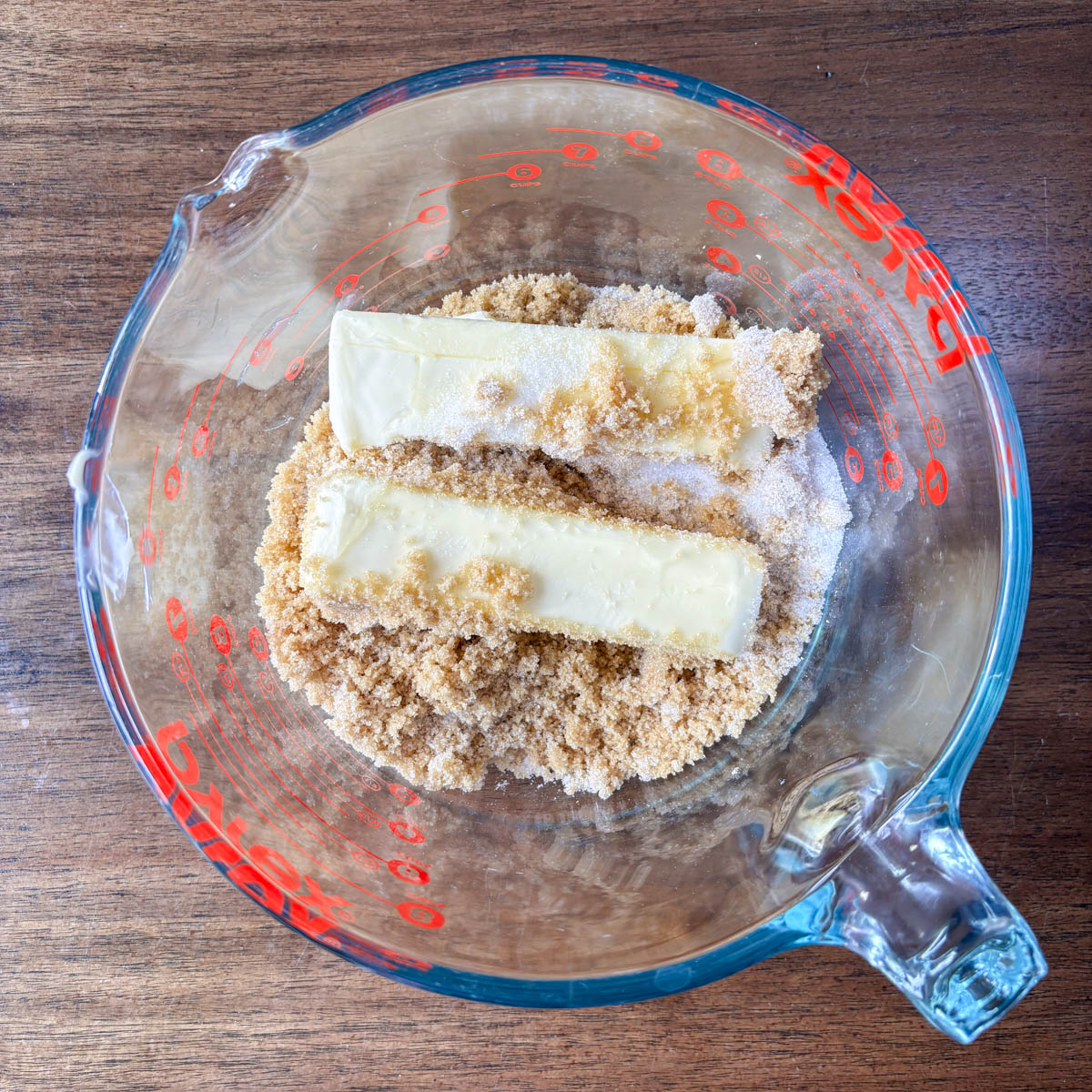 A glass measuring bowl with two sticks of butter, brown sugar, and white sugar sits on a wooden surface—perfect for starting your favorite maraschino cherry cookies.