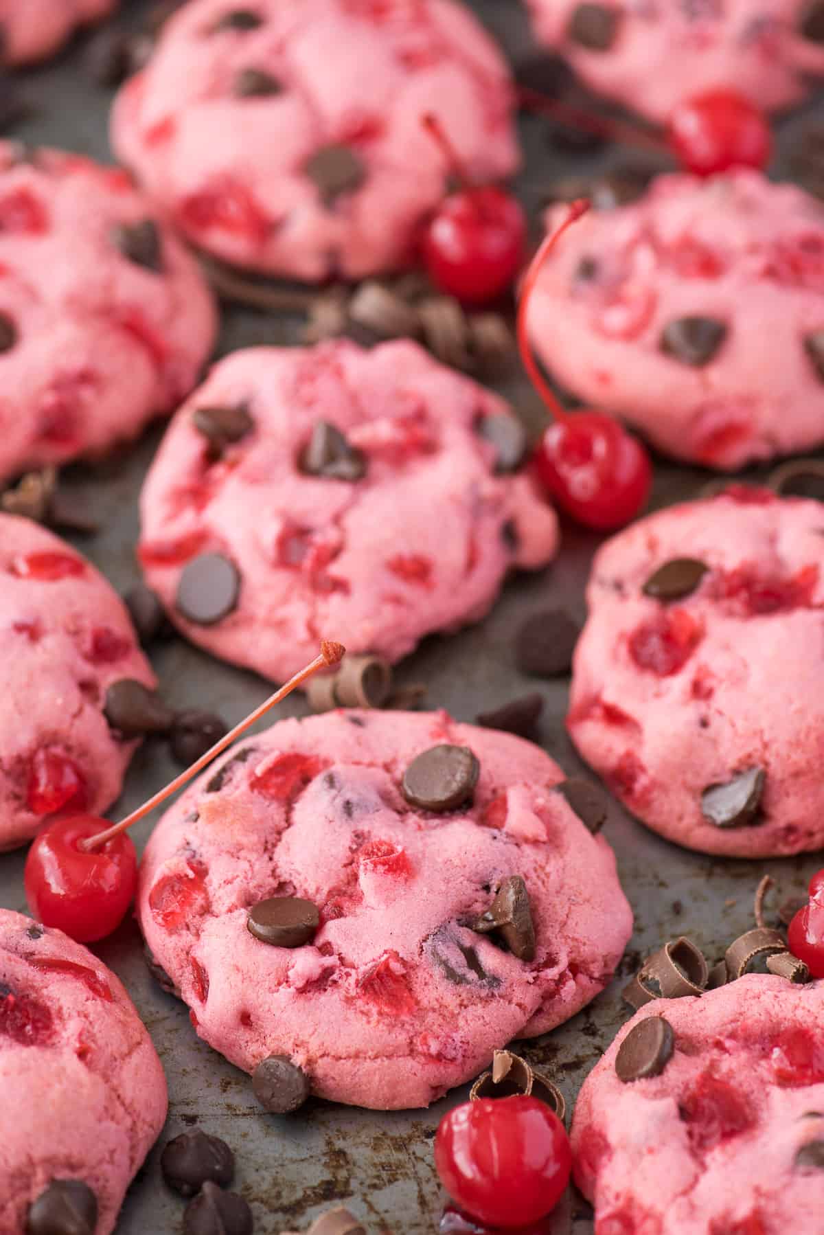 pink maraschino cherry chocolate chip cookies on baking sheet with cherries and chocolate chips