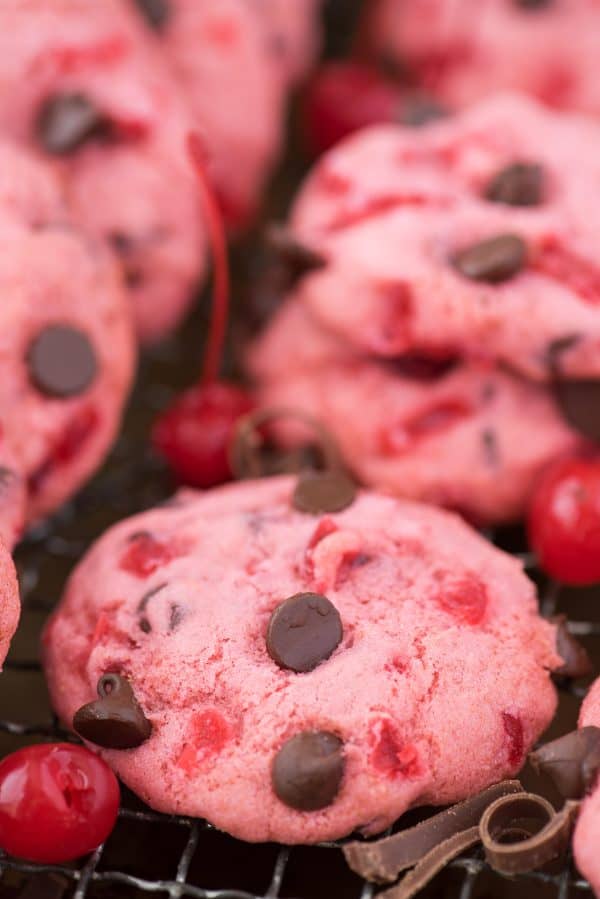 pink maraschino cherry chocolate chip cookies on baking sheet with cherries and chocolate chips