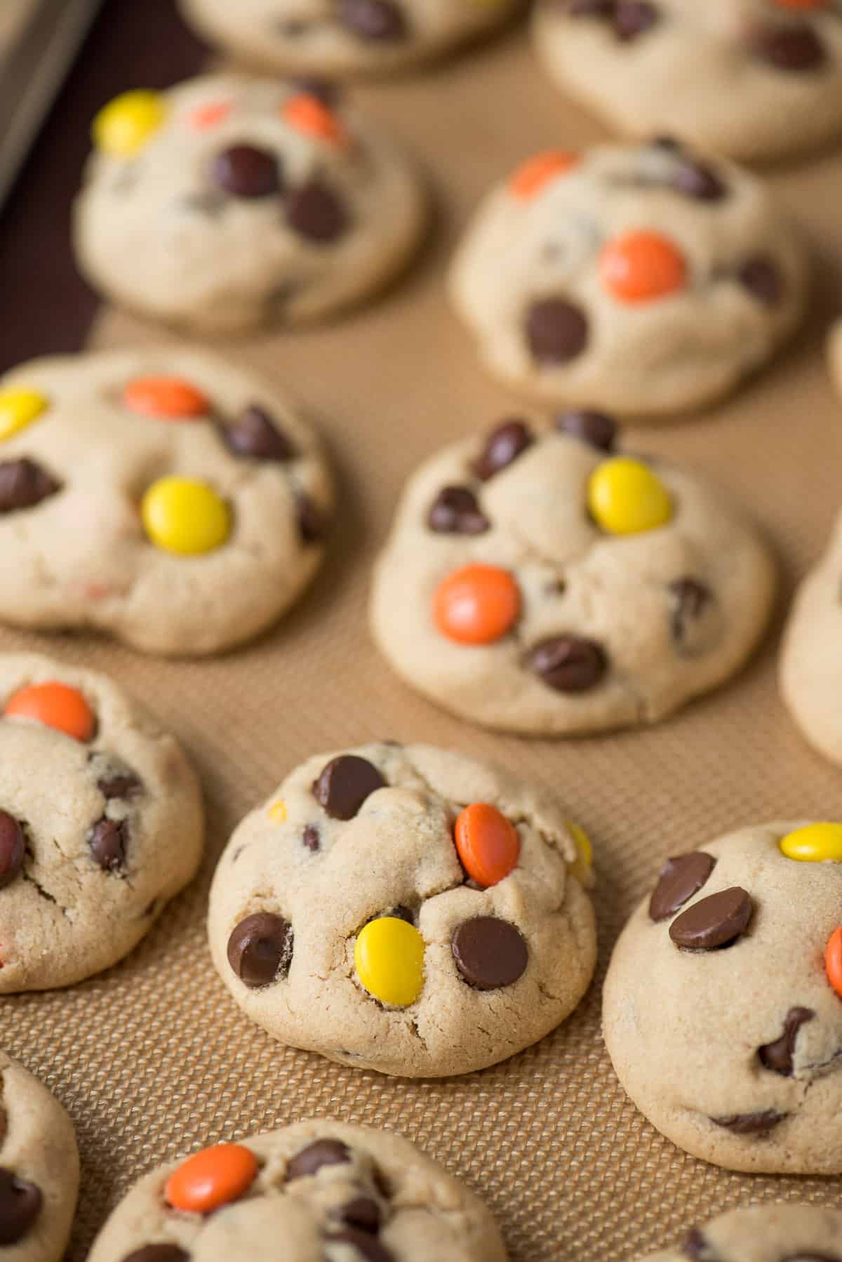 peanut butter cookies with reese's pieces candies and chocolate chips on metal baking sheet