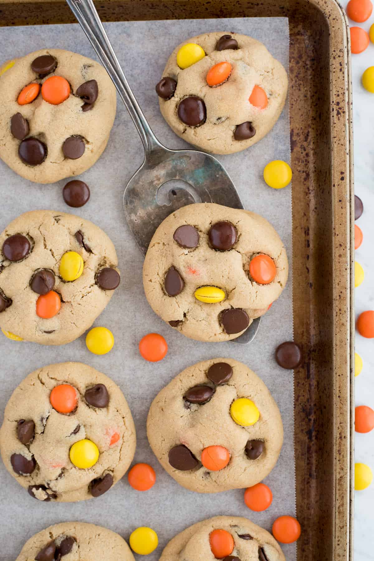 peanut butter cookies with reese's pieces candies and chocolate chips on metal baking sheet