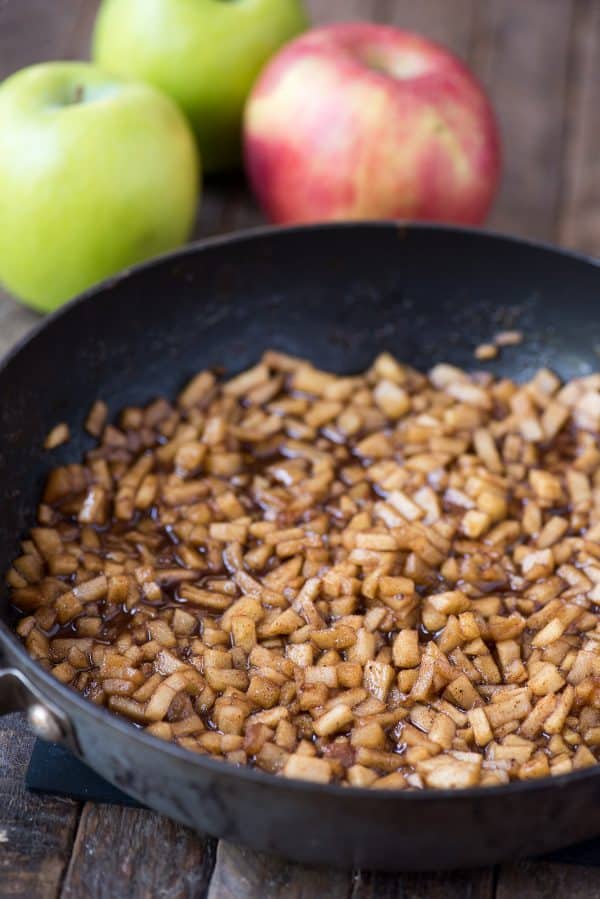 Homemade apple hand pies are a great apple dessert to make any time of the year. Watch the quick step by step video to learn how to make these mini apple pies. #applehandpies #handpies #applepie #minipie apple filling in skillet pan with apples in the background