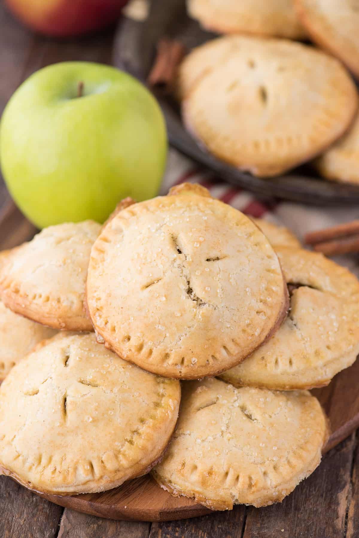 a stack of apple hand pies on wood background with green apple in the background