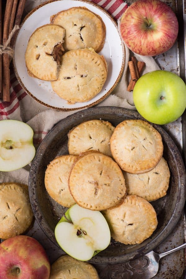 Homemade apple hand pies are a great apple dessert to make any time of the year. Watch the quick step by step video to learn how to make these mini apple pies. #applehandpies #handpies #applepie #minipie apple hand pies on plates with apples and tan colored napkin