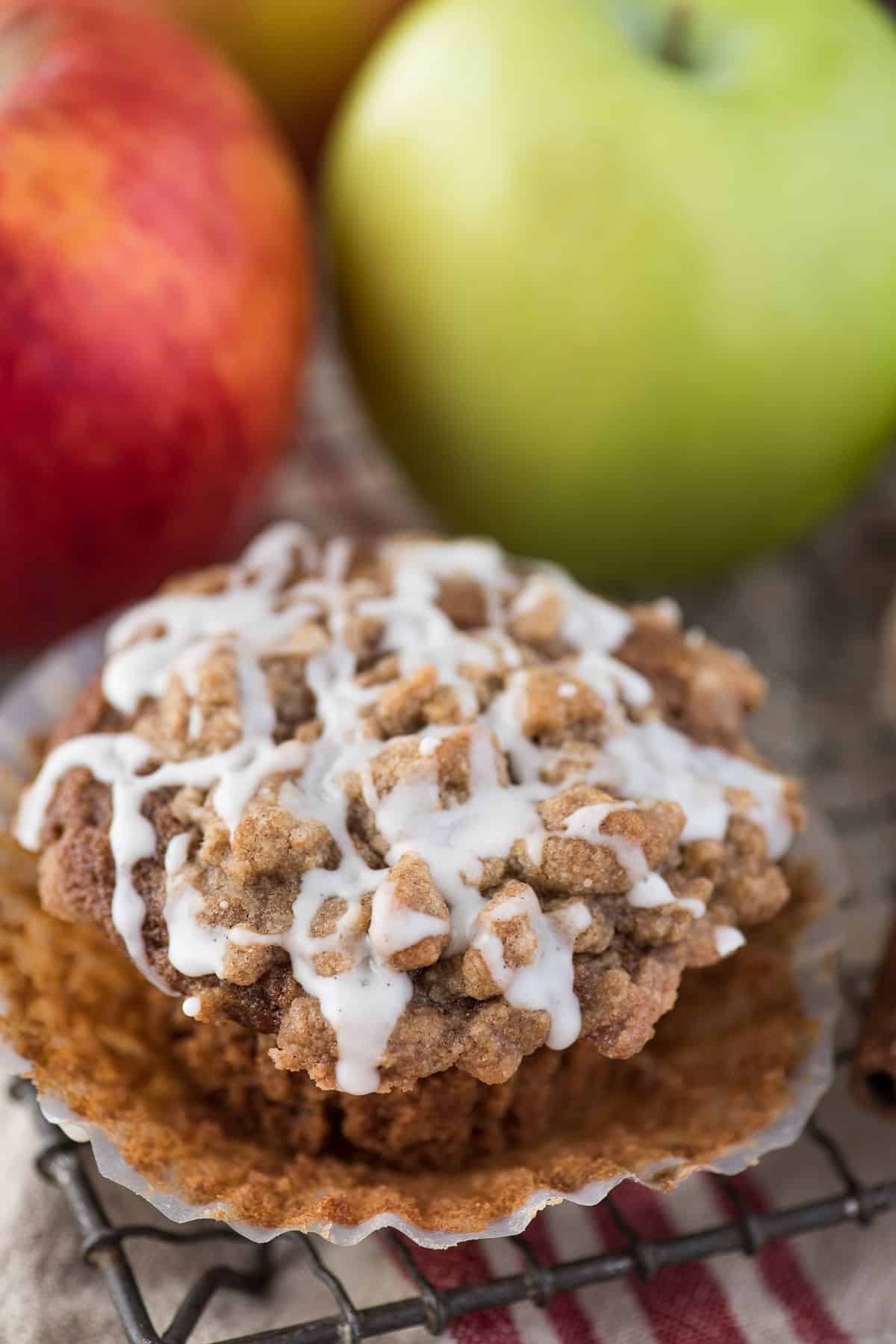 applesauce spice muffins with crumb topping and white glaze on wire rack and apples in the background