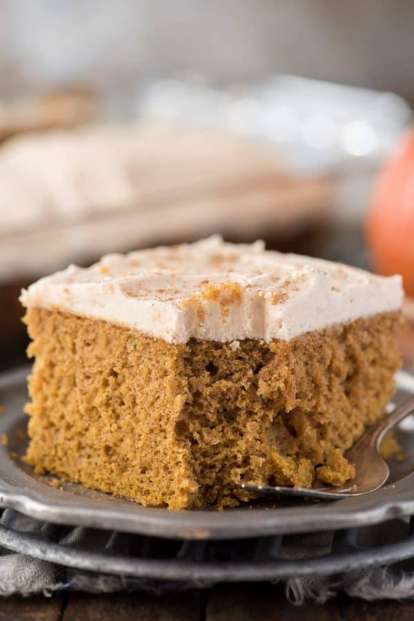 Take a spice cake mix and turn it into a doctored up pumpkin cake! With directions for how to make doctored up pumpkin cake or cupcakes, this is our family’s new favorite pumpkin cake! slice of doctored up pumpkin cake on metal plate with pumpkin in background