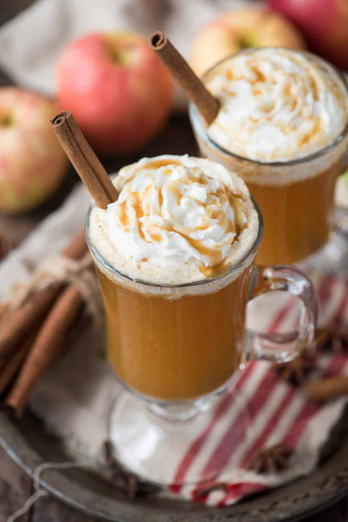 hot apple cider in clear glass with whipped cream and a cinnamon stick