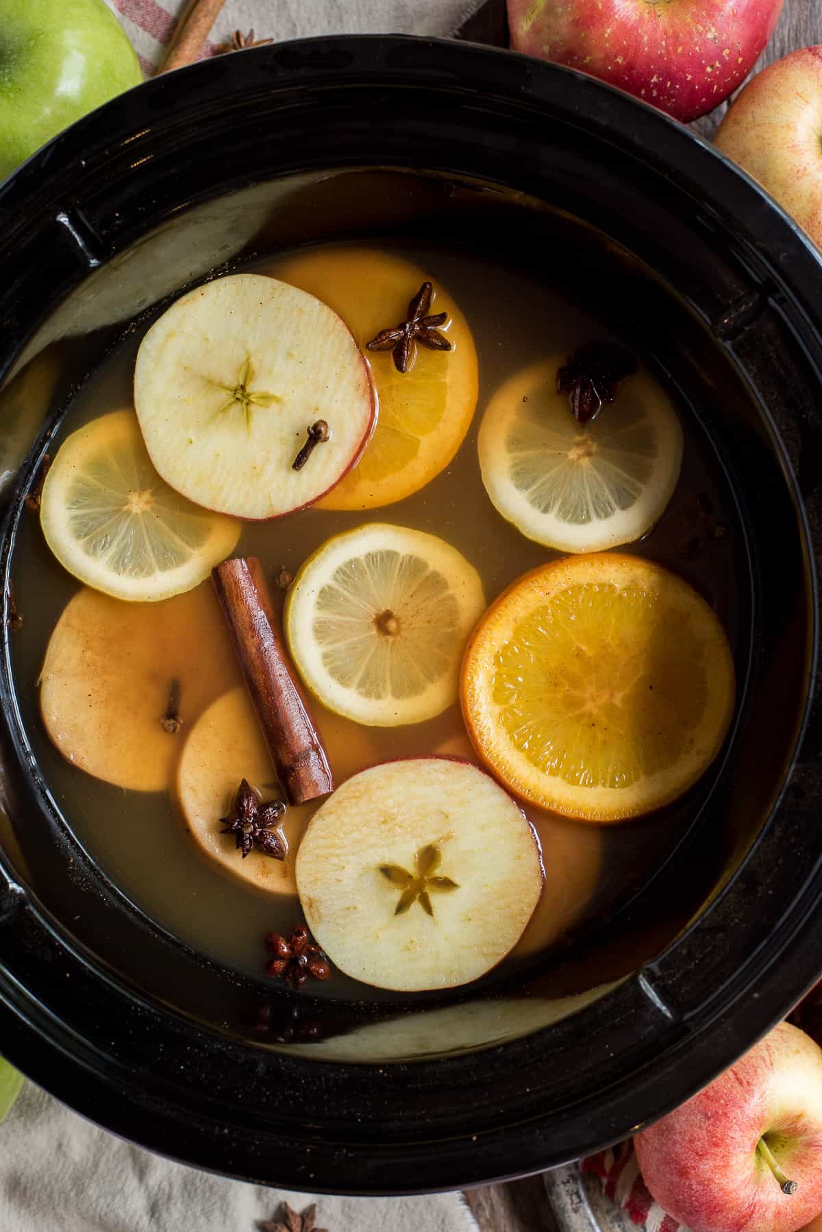 hot apple cider in crock pot with orange, lemon and apple slices and cinnamon sticks 