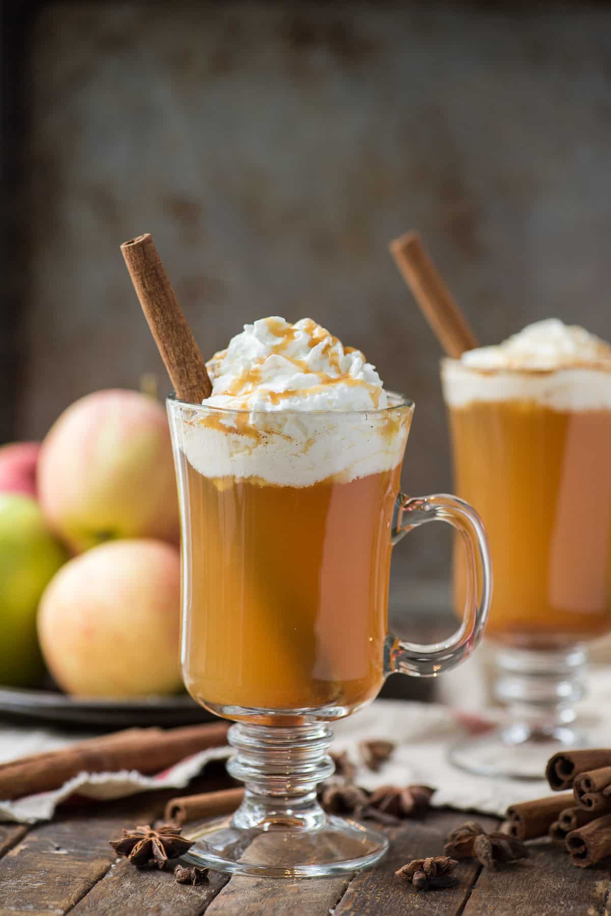 hot apple cider in clear glass with whipped cream and a cinnamon stick