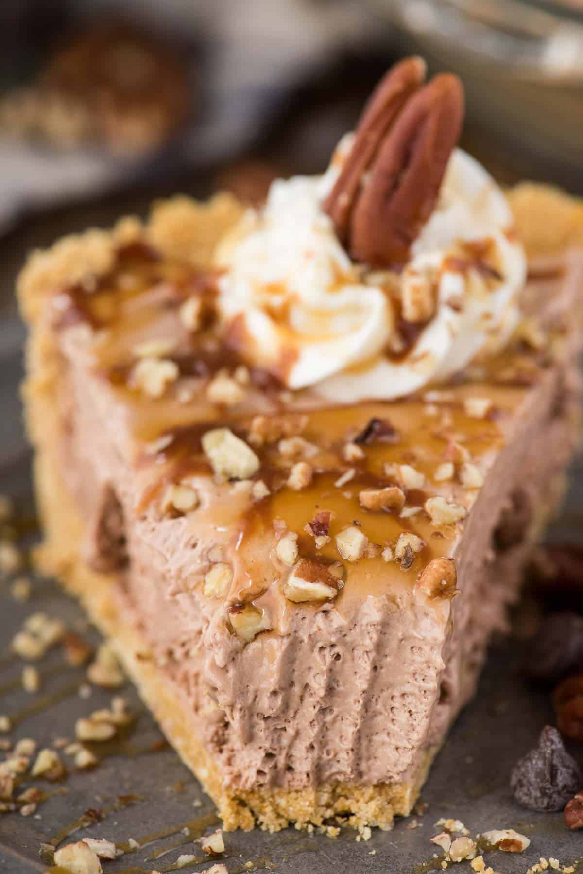 slice of turtle pie with chocolate filling, chopped pecans and caramel drizzle on metal plate