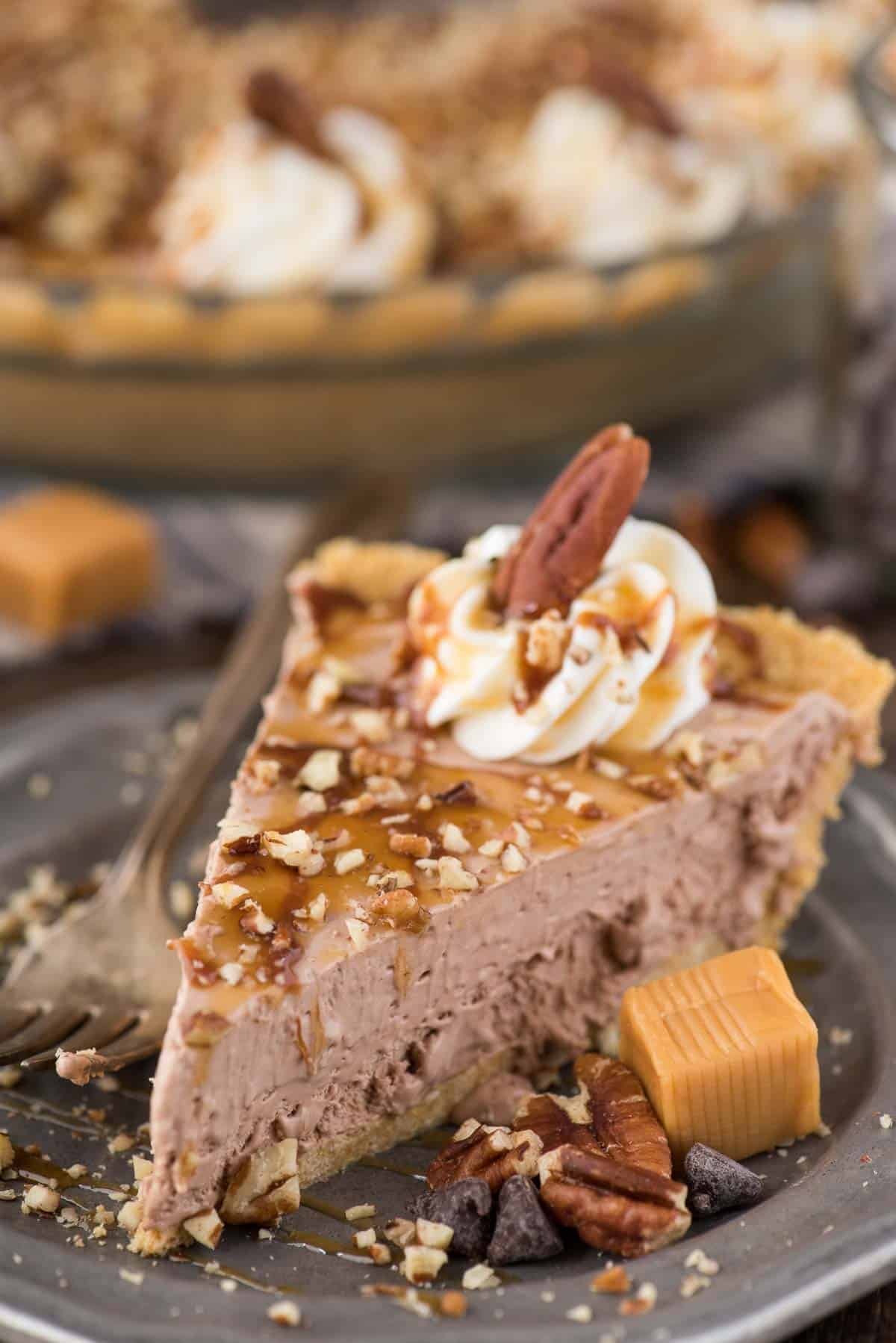 slice of turtle pie with chocolate filling, chopped pecans and caramel drizzle on metal plate