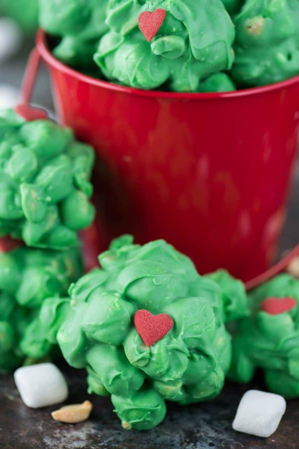 Easy to make Grinch peanut marshmallow candy clusters. These are a family favorite to make each holiday season. Make this grinch candy while watching The Grinch! peanut marshmallow clusters coated in green chocolate with a red candy heart for grinch clusters!