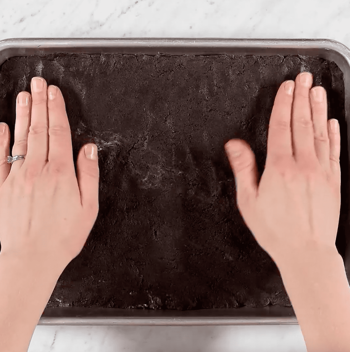 hands pressing oreo ball mixture into pan