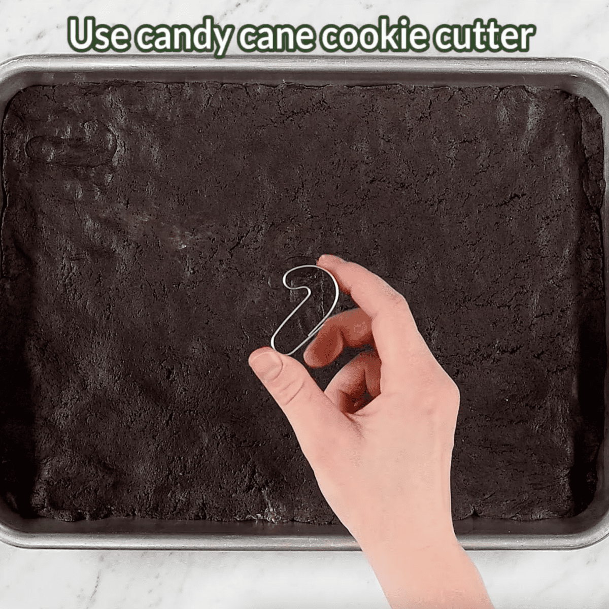 hand holding candy cane cookie cutter over tray of oreo ball dough