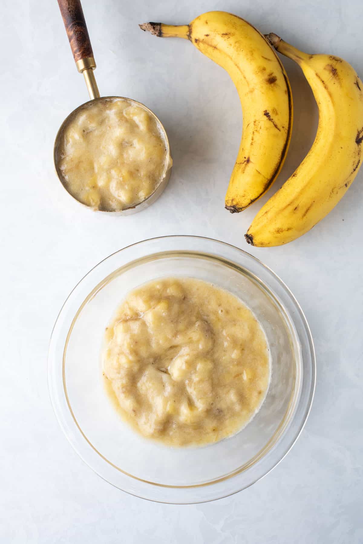 mashed banana in a measuring cup and in a glass mixing bowl