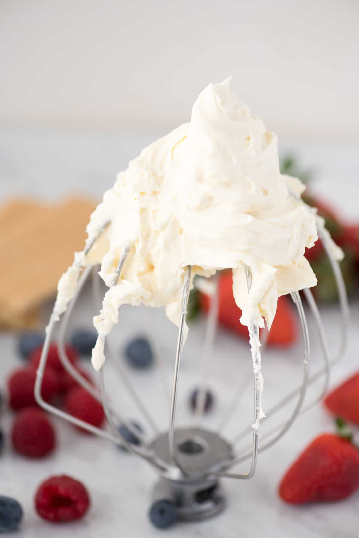 kitchenaid whisk attachment with cheesecake whipped cream on it with berries in background
