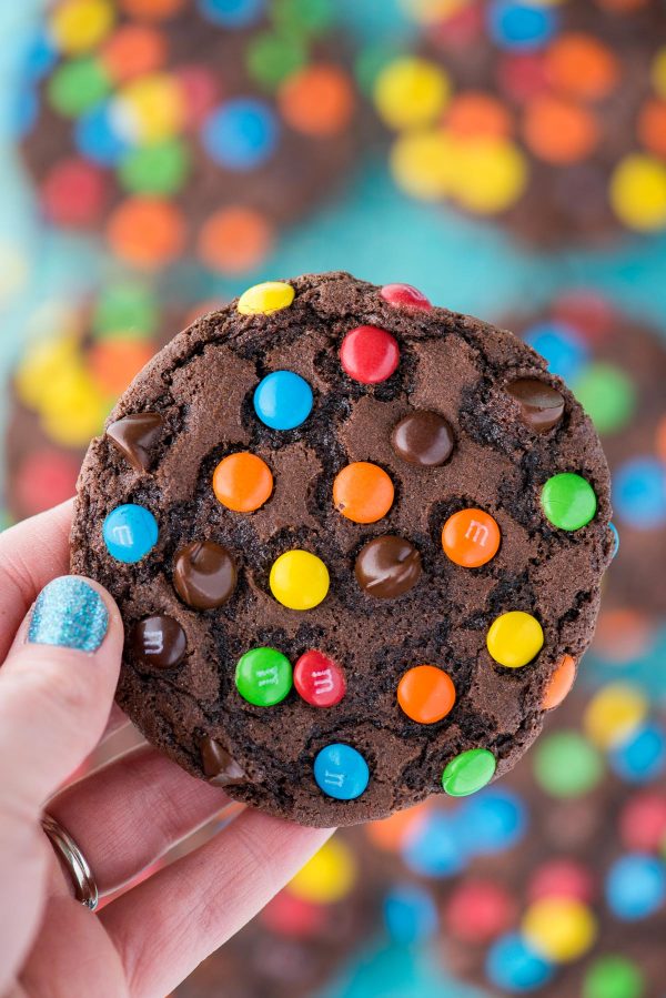 These double chocolate chip M&M cookies are easy to make, only 20 minutes from start to finish. Plus no chilling of the dough! These m&m cookies are chocolate-y, chewy & soft and loaded with m&ms and chocolate chips. #chocolatemmcookies #doublechocolatecookies #mmcookies hand holding double chocolate chip cookie with m&ms and chocolate chips