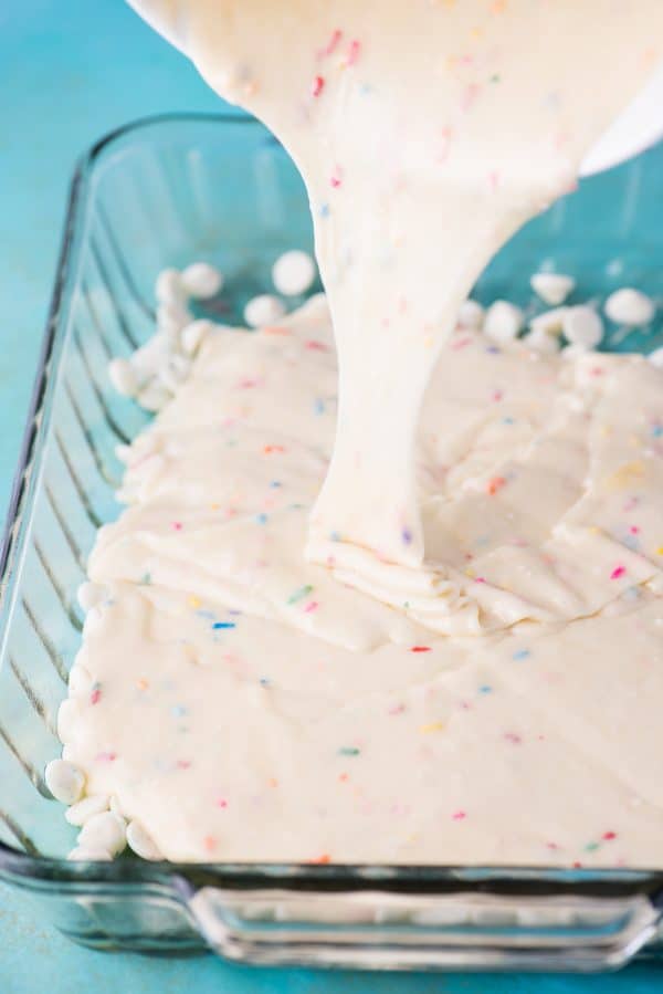 This funfetti earthquake cake is a white cake mix loaded with sprinkles and funfetti chocolate chips. Swirl in the cream cheese frosting layer and it bakes into the cake creating crevices and cracks on top of the cake. #earthquakecake #funfetticake #cake funfett cake mix batter being poured into glass 9x13 inch pan
