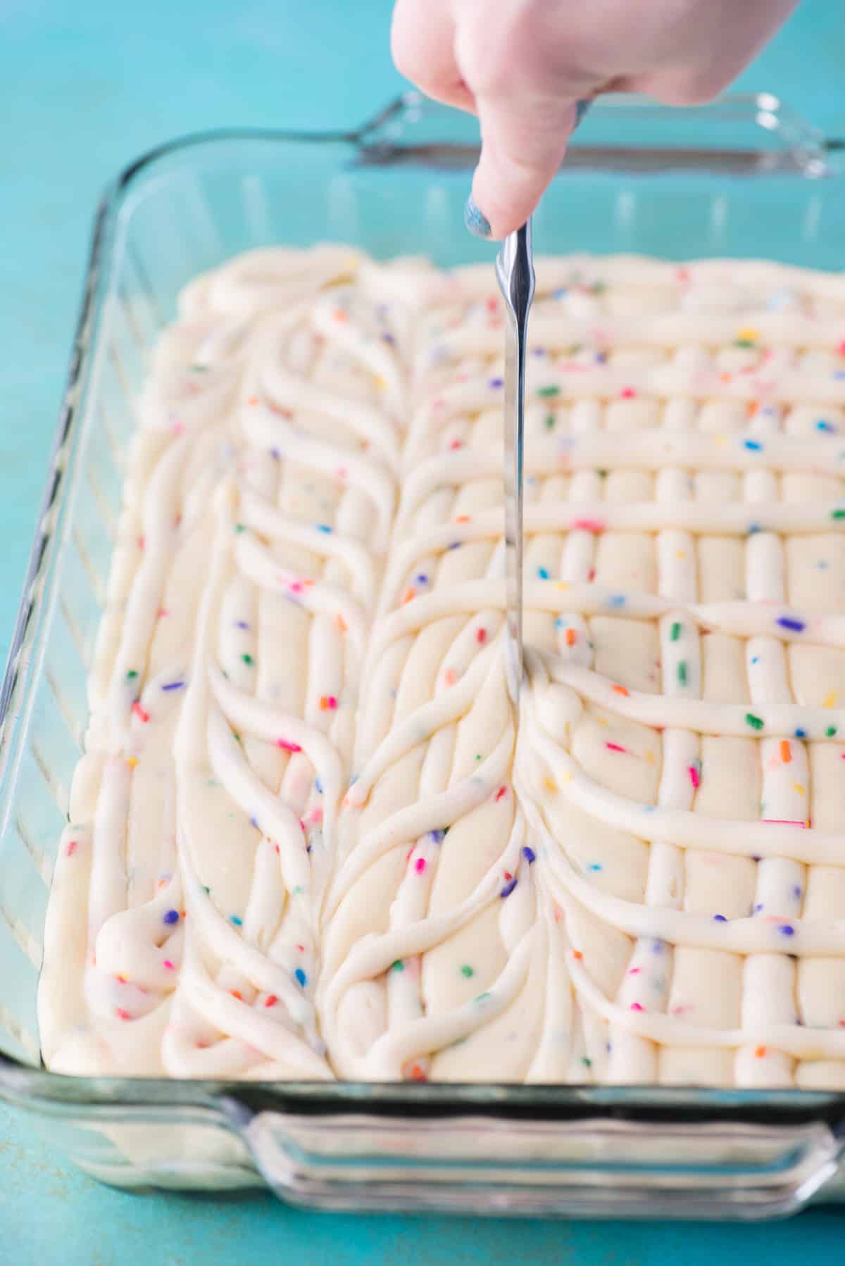 swirling cake batter and cream cheese frosting together with butter knife in glass 9x13 inch pan